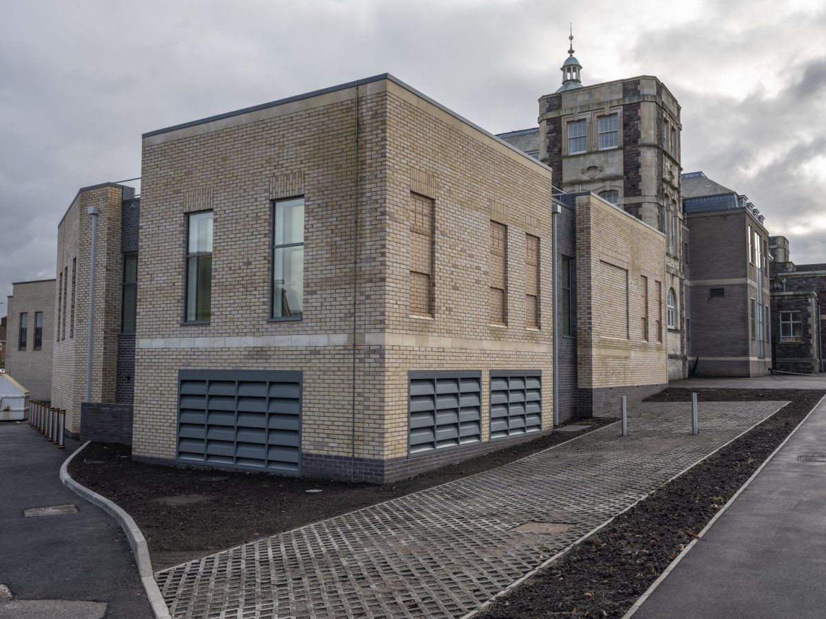 The completed diagnostic imaging extension at Cossham Hospital: pale brick, grey louvres at ground level, with the original hospital tower behind.