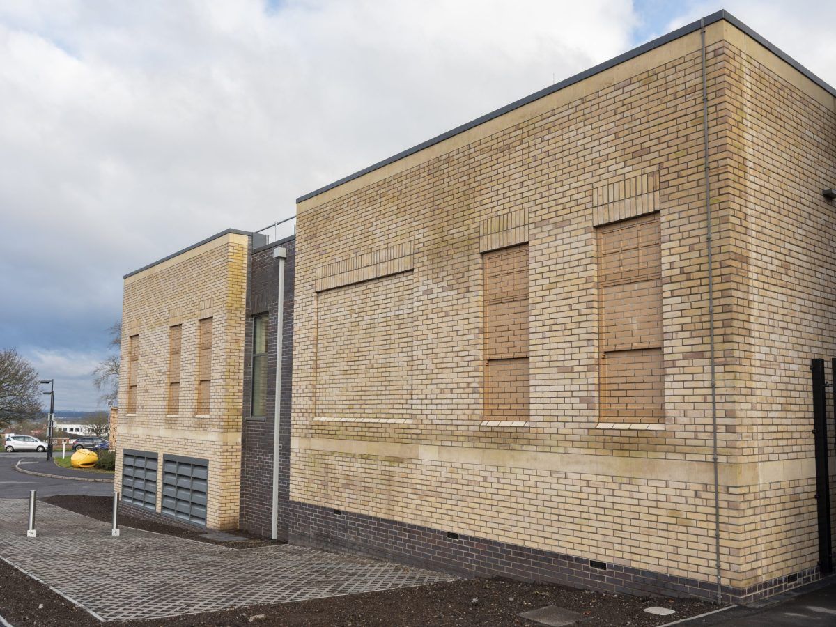 Long brick elevation of the Cossham Hospital imaging extension, with tall windows and a dark brick plinth.